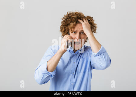 Porträt einer schockiert junger Mann mit lockigem Haar auf weißem Hintergrund, Gespräch am Handy Stockfoto