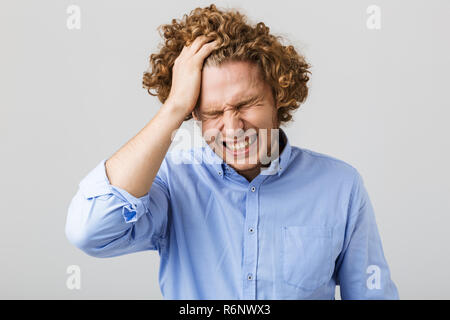 Porträt einer betont jungen Mann mit Hemd stehend über grauen Hintergrund isoliert, leiden unter Kopfschmerzen Stockfoto