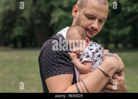 Junger Vater außerhalb schaukelnd seine niedlichen Baby Boy Stockfoto