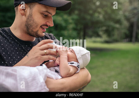 Lächelnd Vater, der sein Baby Boy außerhalb Füttern mit der Flasche Stockfoto