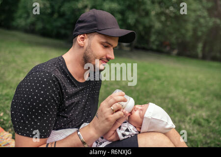 Vater draußen Fütterung sein baby Junge mit einer Flasche Stockfoto