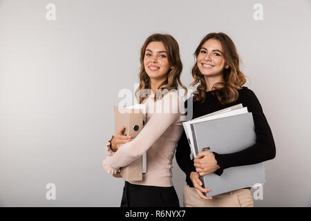 Bild von zwei jugendlichen Frauen und lächelnd Ordner über grauer Hintergrund Stockfoto