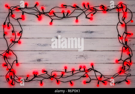 Eine Zeichenkette von roten Holly berryr Weihnachtsbeleuchtung, auf einem destressed woodern Hintergrund, Schaffung eines Rahmens um einen leeren Raum für Kopie Stockfoto
