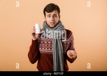 Porträt eines kranken Mann in Pulli und Schal bekleidet isoliert über beigen Hintergrund, halten Sie Flasche und Pillen Stockfoto