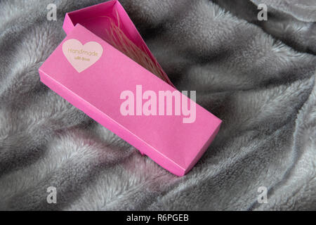 Big Pink Geschenkbox mit einem Herz voller Liebe auf das Silber Grau flauschigen Fellimitat decke Hintergrund geöffnet. Label Handarbeit mit Liebe am Herzen. Straußenfedern Ohrringe in Box Stockfoto