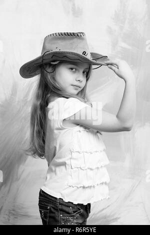 Kleines Mädchen in Cowboy oder Cowgirl Outfit mit erhobener Hand Hut auf farbigen Hintergrund Stockfoto