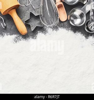 Küchengeräte und Mehl zum Backen oder kochen Hintergrund. Rolling Pin, Schneebesen, Löffel aus Holz, Ausstechformen und Messlöffel auf Dunkelgrau concre Stockfoto