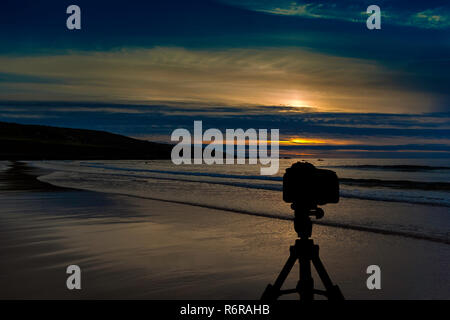Kamera auf Stativ mit Sonnenuntergang über dem Meer im Hintergrund Stockfoto