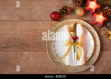 Weihnachtsfeiertag abends Einstellung - Platten, Serviette, Besteck, gold Christbaumkugel Dekorationen über Eiche Tisch Hintergrund. Gabel und Löffel auf goldenen Platten. Ar Stockfoto