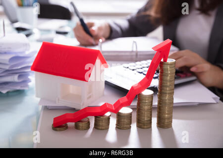 Gestapelte Münzen und Pfeil vor Haus Modell Stockfoto