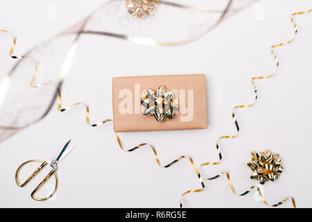 Flach Geschenkbox in braunem Papier mit Gold Bug verpackt neben Schere und Bänder auf weißem Hintergrund, Ansicht von oben. Stockfoto
