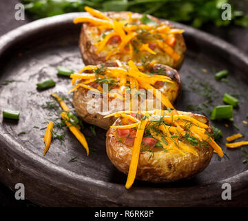 Gebackene gefüllte Kartoffeln mit Käse, Schinken, Schnittlauch, Dill und Gewürze auf dunklem Hintergrund Stockfoto