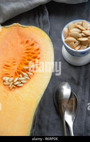 Kürbis in Scheiben geschnitten in der Hälfte auf eine Tabelle mit Samen in einer Tasse. curcubita moschata für das Abendessen vorbereitet Stockfoto