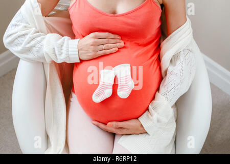 Bauch der weissen Kaukasischen schwangere Frau mit niedlichen kleinen neugeborenen Socken, die Aussicht von oben über. Erwartet weiblich Dame im Sessel halten berühren Stockfoto