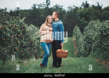 Glückliche gesunde Schwangerschaft und Elternschaft. Portrait von Schwangeren junge blonde kaukasische Frau mit Mann auf Apple Farm. Schöne erwartet Mutter und Fu Stockfoto