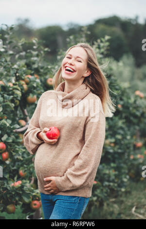 Glückliche gesunde Schwangerschaft. Portrait von Lachen schwangere junge blonde kaukasische Frau auf Apple Farm mit Weidenkorb. Schöne erwartet Mama Dame in Stockfoto