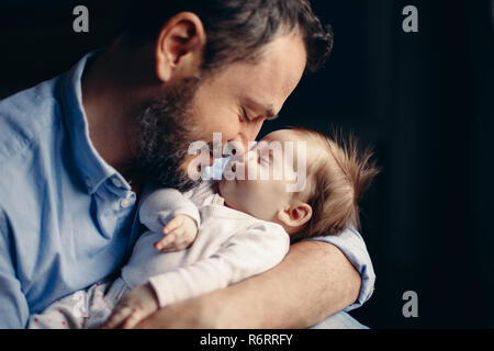 Closeup Portrait von mittleren alter bärtiger Kaukasischen Vater Umarmen und Küssen neugeborenes Baby. Mann Elternteil mit Kind. Authentischen Lebensstil berühren Stockfoto