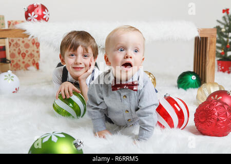 Portrait von weissen Kaukasischen Kinder Brüder zusammen Festlegung unter Holzbank Lachen, feiern Weihnachten oder Neujahr. Kleinen Niedlichen jungen Geschwister Stockfoto