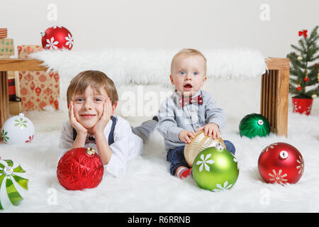 Portrait von weissen Kaukasischen Kinder Brüder zusammen Festlegung unter Holzbank Lachen, feiern Weihnachten oder Neujahr. Kleinen Niedlichen jungen Geschwister Stockfoto