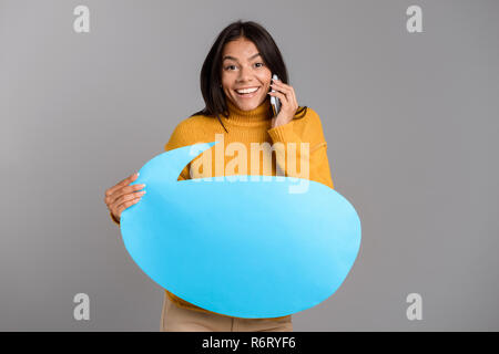 Portrait Of Happy and junge Frau über grauer Hintergrund isoliert, Gespräch am Handy, leere Sprechblase Stockfoto