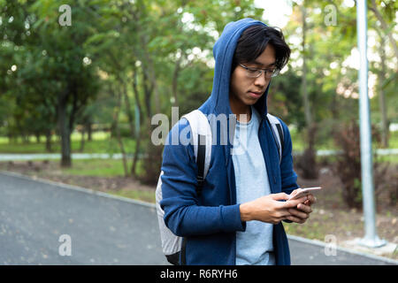 Bild von jungen asiatischen Kerl in Freizeitkleidung und Brillen mit Smartphone bei einem Spaziergang durch den Green Park Stockfoto