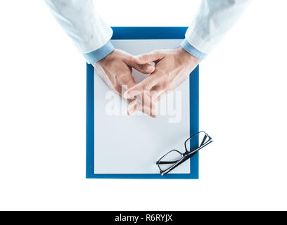 Doktor mit gefalteten Händen warten am Schreibtisch Stockfoto