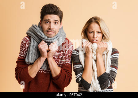 Porträt eines jungen Paares im Pullover und Schals zusammen über beigen Hintergrund stehen isoliert gekleidet, schütteln Stockfoto
