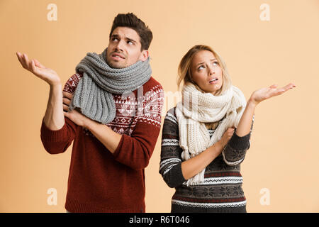 Porträt eines jungen Paares im Pullover und Schals zusammen über beigen Hintergrund stehen isoliert, Schütteln, ausgestreckten Händen gekleidet Stockfoto