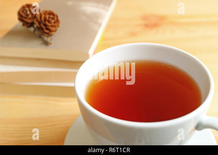 Geschlossen, eine heiße Tasse Tee am Holztisch mit unscharfen Stapel von Büchern und trockene Tannenzapfen oben im Hintergrund Stockfoto
