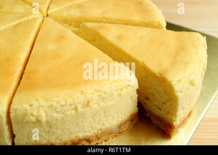 Geschlossen, ein Stück der Cremegelben plain gebackene Käsetorte Schnitt von den ganzen Kuchen Stockfoto