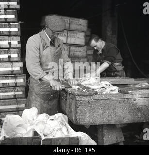 1950, historische, qualifizierte männliche Arbeiter außerhalb Billingsgate Fish Market in London Filetieren frischen Fisch kam neulich in Kisten vom Rumpf. Stockfoto