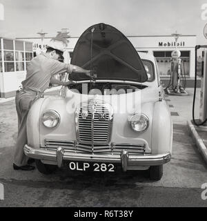 1950, historische, ein Auto der Ära an den Zapfsäulen mit seiner Motorhaube öffnen bei einem Ölwechsel von einem uniformierten Tankwart, England, UK. In dieser goldenen Ära des Autofahrens, viele Garagen oder was nannte man 'Service-Stationen' spezialisiert hatte Attendants sowie Betanken des Autos würde auch routinemäßige Wartungsarbeiten bieten und die Fahrzeuge Öl, Wasser und Reifendruck prüfen. Stockfoto