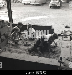 1960er Jahre, eine Gruppe von Jungen, die zusammen spielen in einem behelfsmäßigen Sandkasten draußen an einem builders Yard oder Depot, England, UK. Stockfoto