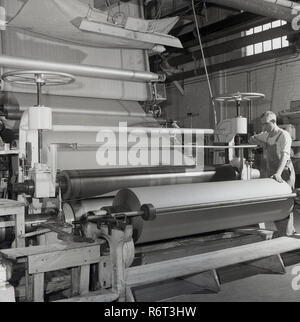 1950, historische, Brittains Papierfabrik, ein männlicher Arbeiter in der Fabrik die Beaufsichtigung der Arbeiten einer großen industriellen Maschinen, eine Rolle, wo die Blätter der hergestellten Papier auf fertig sind. Stockfoto
