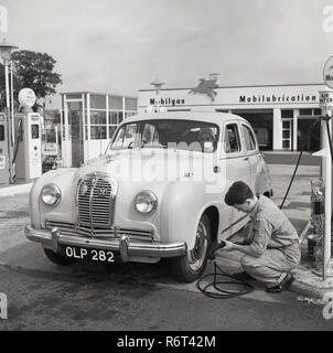 1950, historische, die goldenen Tage des Autofahrens, ein junges Männchen Service Station sttendant prüft den Reifendruck auf einem Austin Auto an einem kraftstoffpumpen an einem Mobilgas Service Station, London, England, UK geparkt. Stockfoto