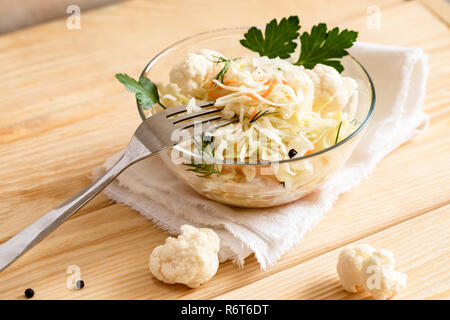 Sauerkraut in Glasschale mit Gabel steht auf weisse Serviette auf Holztisch. Stockfoto