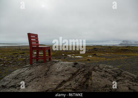 Eine hölzerne großen roten Stuhl, der auf einem Felsen am Meer in der Nähe von Eystrahorn, East Iceland Stockfoto