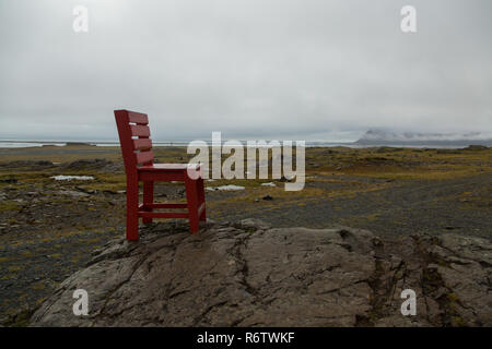 Eine hölzerne großen roten Stuhl, der auf einem Felsen am Meer in der Nähe von Eystrahorn, East Iceland Stockfoto