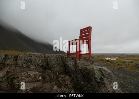 Eine hölzerne großen roten Stuhl, der auf einem Felsen am Meer in der Nähe von Eystrahorn, East Iceland Stockfoto
