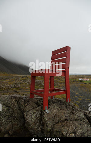 Eine hölzerne großen roten Stuhl, der auf einem Felsen am Meer in der Nähe von Eystrahorn, East Iceland Stockfoto