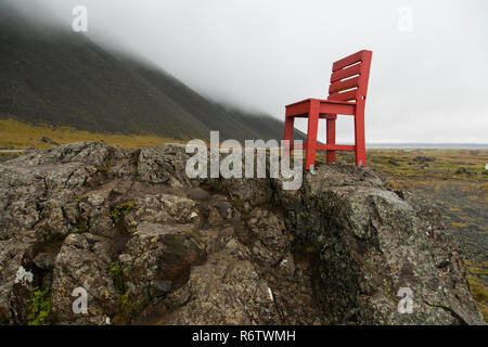 Eine hölzerne großen roten Stuhl, der auf einem Felsen am Meer in der Nähe von Eystrahorn, East Iceland Stockfoto