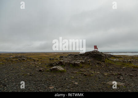 Eine hölzerne großen roten Stuhl, der auf einem Felsen am Meer in der Nähe von Eystrahorn, East Iceland Stockfoto