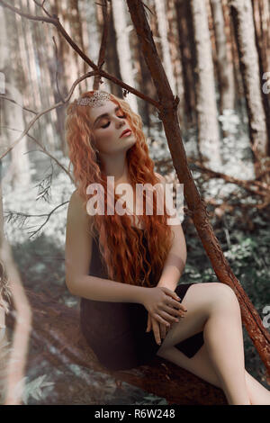 Romantische Frau mit roten Haaren im Gras in den Wäldern liegen. Ein Mädchen in einem leichten schwarzen Kleid schläft und träumt in einem magischen Wald Stockfoto