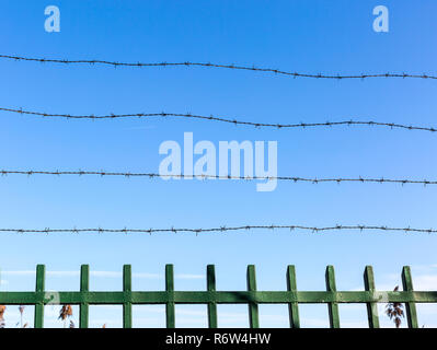 Stacheldraht auf Zaun gegen den blauen Himmel. Symbol der Unfreiheit und Entbehrung. Unfreiheit Konzept. Stockfoto