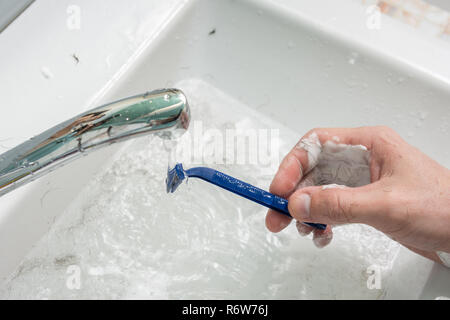 Die Hand des Mannes wäscht den Rasierer unter fließendem Wasser, close-up auf der Oberseite Stockfoto