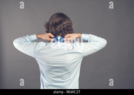 Herr Perfektion. Ansicht der Rückseite des stattlichen shaggy lockigen Jungen Mann mit blauem Hemd sein Bow Tie während zurück gegen grauen Hintergrund stehen. Elegant gekleideten Kerl. Getönt. Für text Stockfoto