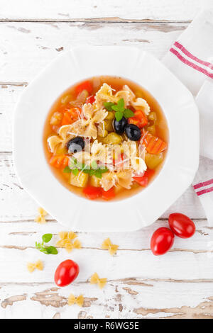 Minestrone, vegetarische Suppe mit Nudeln und Gemüse auf weißen Holzmöbeln rustikal Hintergrund. Traditionelle italienische Küche. Ansicht von oben Stockfoto