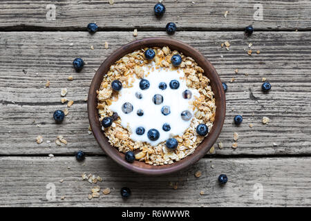 Schüssel Hafer Müsli mit Joghurt, frischen Blaubeeren auf rustikalen Holzbrett für gesundes Frühstück, Ansicht von oben Stockfoto