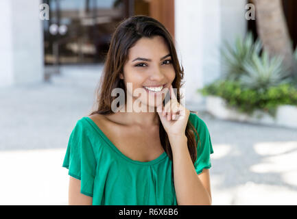 Attraktive lateinamerikanischen junge erwachsene Frau in grün Shirt im Sommer in der Stadt Stockfoto