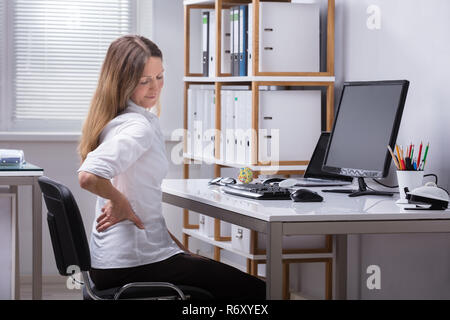 Seitliche Sicht auf eine Geschäftsfrau mit Rückenbeschwerden Stockfoto